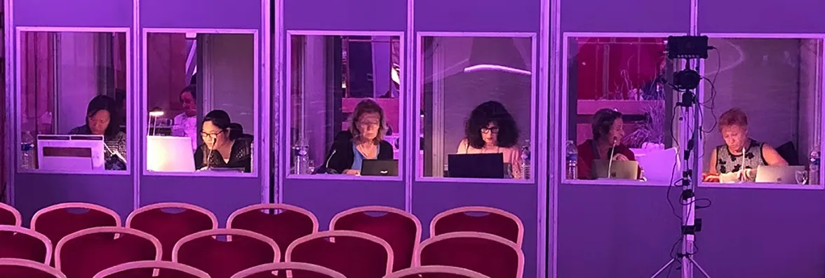 Trois cabines d'interprétation vitrées en fond de salle, interprètes SOGEDICOM au travail pendant une conférence